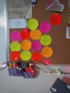 Blurry image of a bulletin board with multi-colour stars, cards and photos